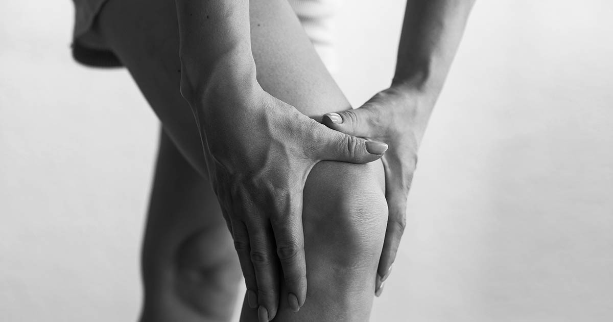 Older adult holding an aching knee while a Lakewood Ranch chiropractor examines the joint before non-surgical knee pain treatment