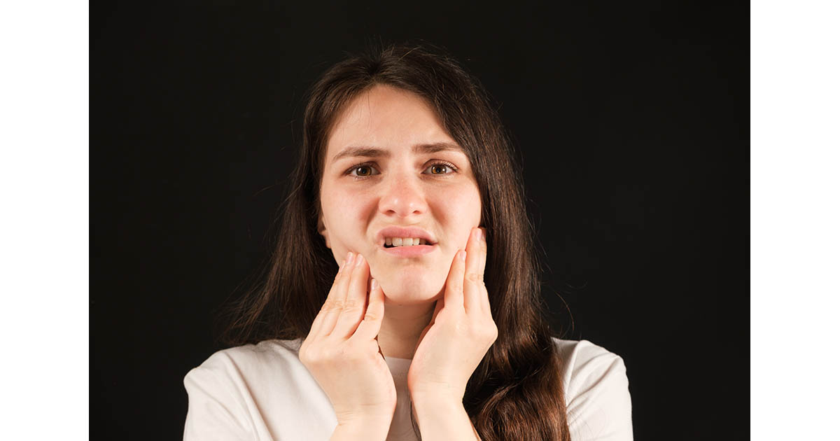 Woman holding the side of her jaw in discomfort, illustrating TMJ jaw pain treated at Spine and Wellness Center Lakewood Ranch